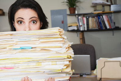woman peering from behind a large stack of files