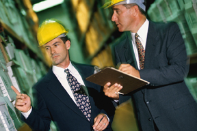two business men wearing hard hats as they walk through a warehouse